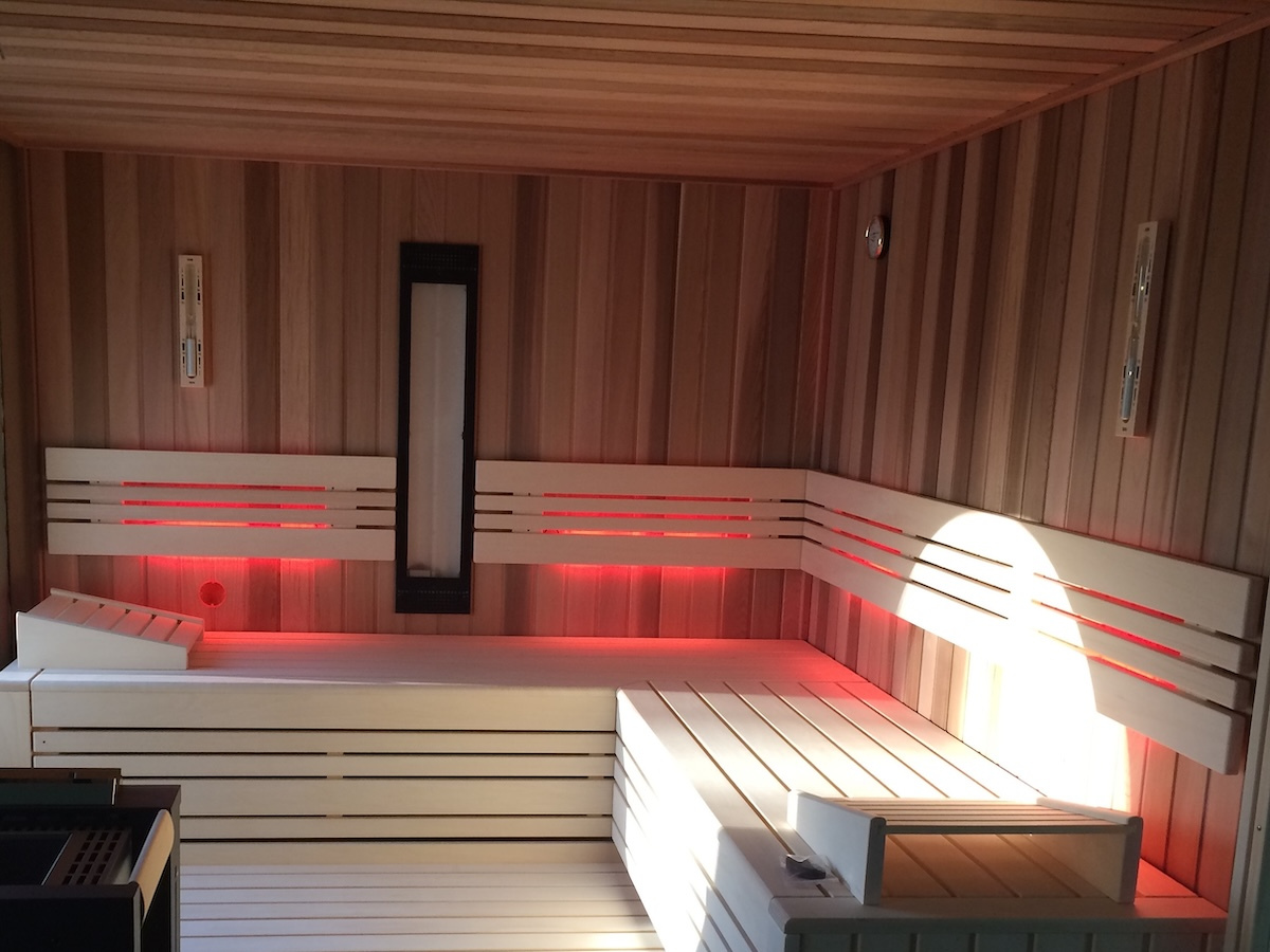 Exklusive Sauna in Zedernholz-Verkleidung, rundem Aussenfenster, helle Saunabänken in Espe, sowie LED-Farblicht hinter de Rückenlehnen